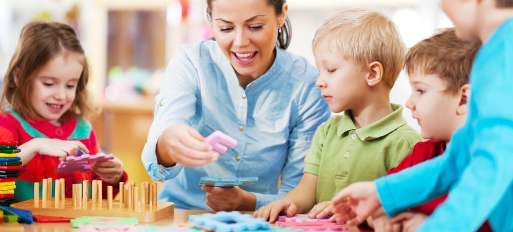 Dans une garderie, une femme s'occupe d'enfant à une table. Ils font des puzzles ensemble. 