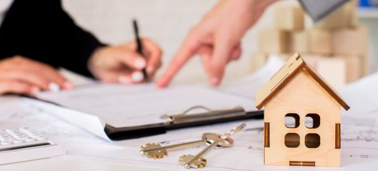 Maquette de maison en bois avec des clés à côtés et en arrière plan des personnes qui signent un papier 