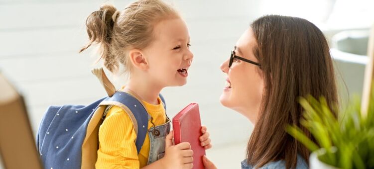 Une mère agenouillée au niveau de sa petite fille allant à l'école