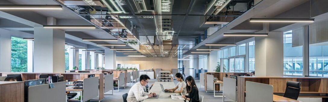 Trois personnes travaillant sur une table entourée d'autres bureaux semi-cloisonnés dans un grand open-space