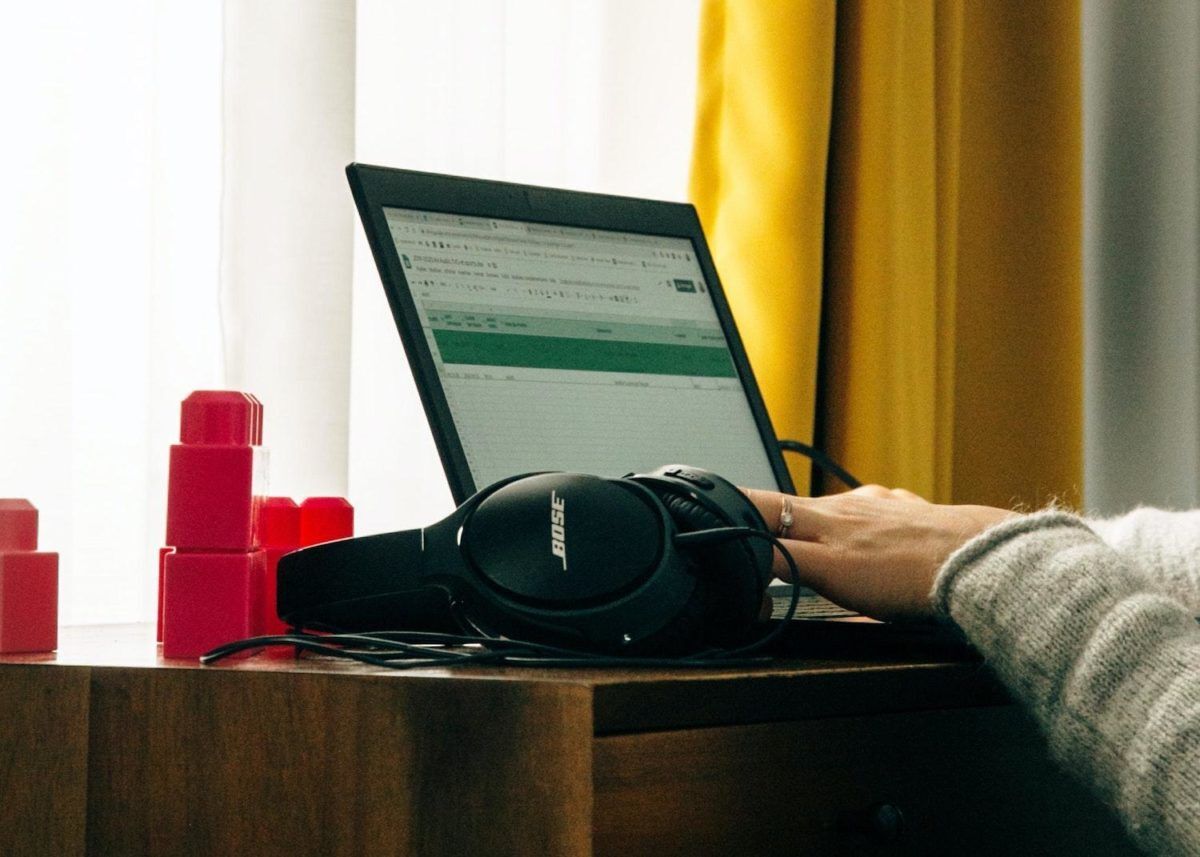 Main tapant au clavier sur un ordinateur portable avec un casque audio posé à sa gauche