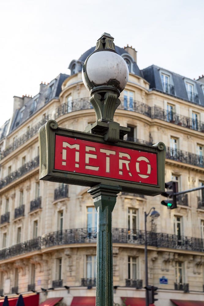 Panneau de bouche de métro avec façade haussmannienne en fond