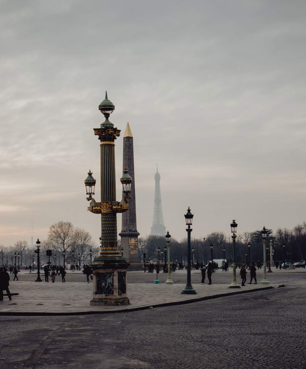 Un des lampadaire de la place concorde se trouve au premier plan, au deuxième, l'obélisque, au troisième plan légèrement masquée par le brouillard, la tour Eiffel