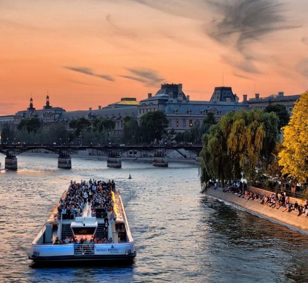 Bateau sur la seine, le ciel est orangé et sur la rive gauche se trouvent des arbres et bâtiments